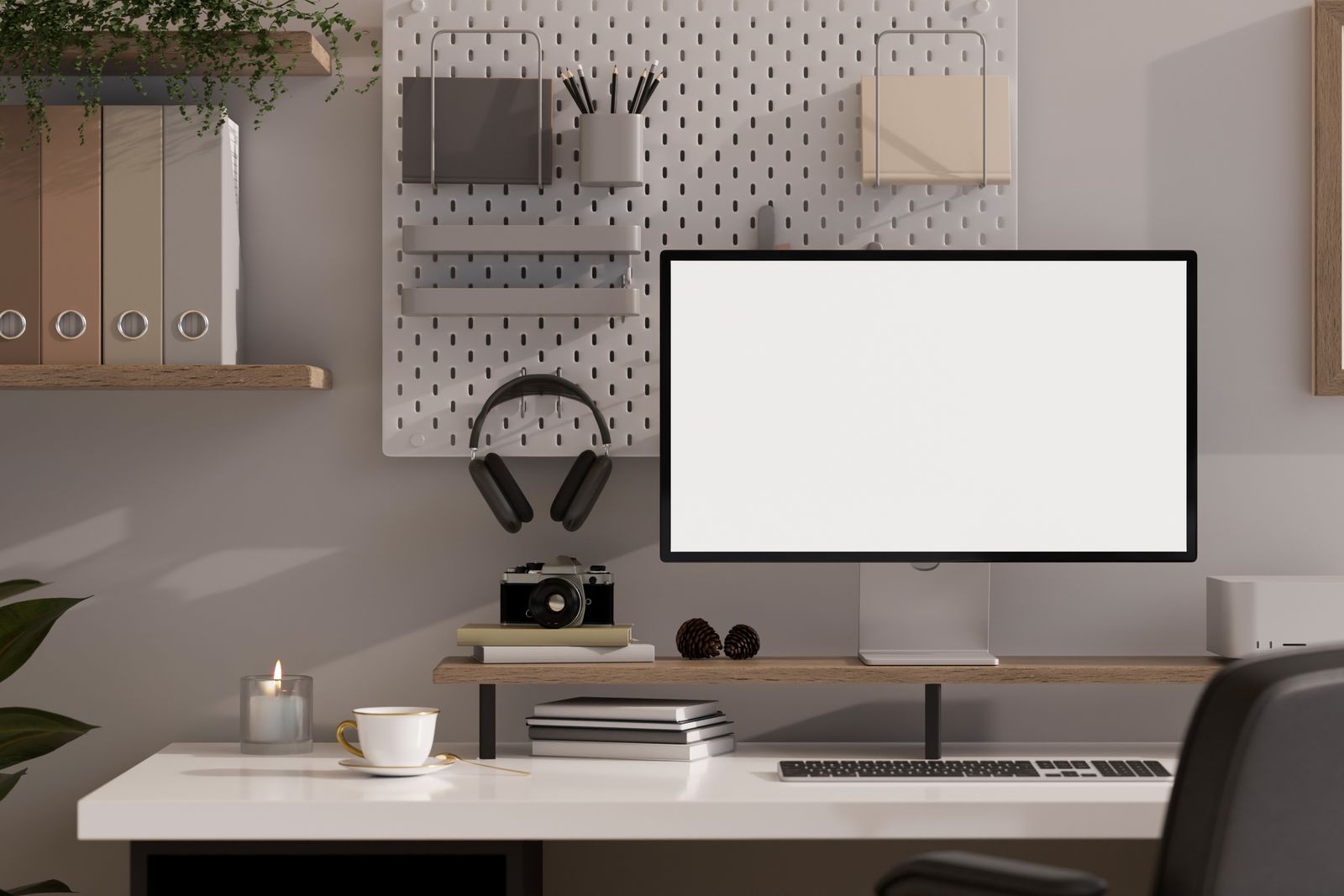 Schreibtisch mit weißer Platte vor einer grauen Wand, Monitor auf einer Holzablage mit der Tastatur darunter, daneben Kamera, Bücher und eine Tasse; an der Wand eine Lochwand mit Kopfhörern, Stiften und Ablagen und ein Regal mit Ordnern